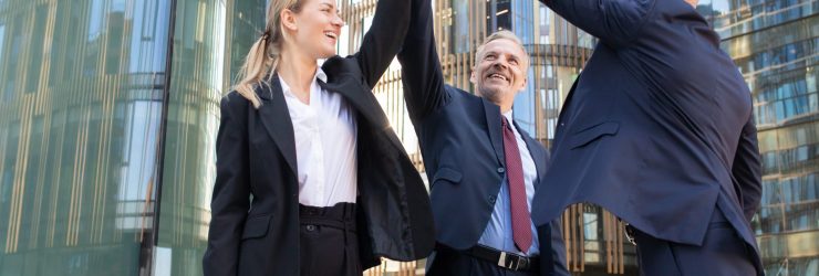 Three cheerful businesspeople giving five and smiling. Confident happy colleagues celebrating successful deal together, standing outdoors and rising hand up. Teamwork and partnership concept